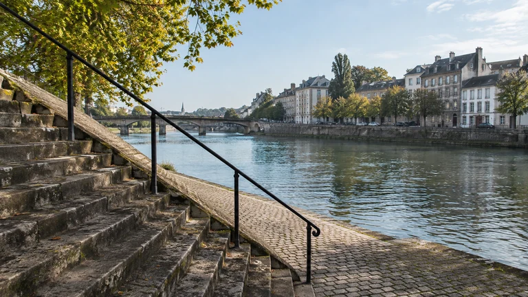 Un large escalier de pierre descend vers un quai arboré au bord de l’eau. Illustration générée par IA pour rbreak.com.